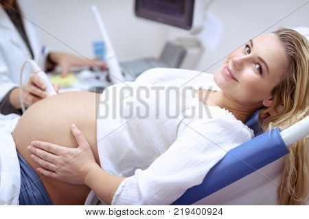 Happy pregnant female visiting women's doctor in the maternity center, with pleasure doing ultrasound scan, checking health of the child, healthy motherhood concept