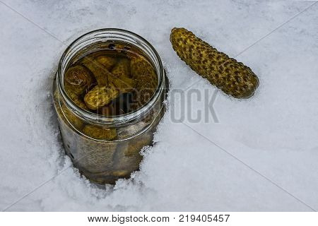 An open glass jar with canned cucumbers in a snowdrift