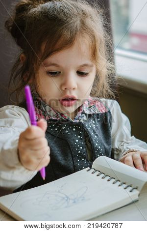 Little kid girl writing or drawing with pen in scetch book.