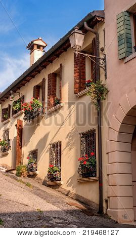 Cozy little street in Conegliano. Windows with blinds are decorated with flowers. The street rises steeply upwards.