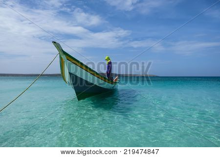Fishing boat with a hooded sailor man anchored next to the coast of Cubagua island (Cubagua island, Venezuela).