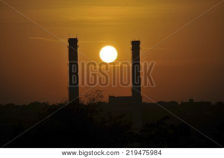 Industrial smoke from chimney at sunset. The sun between the two pipes of the power plant.