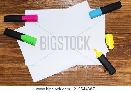 A white sheet of paper lay on a wooden table, near , pencils, markers, pens . The view from the top