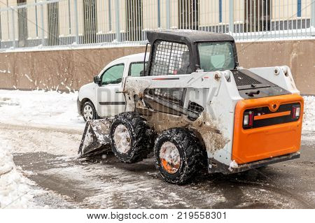 Small tractor loader machine clean  and load snow and ice into a truck from a city streets after heavy snowfall