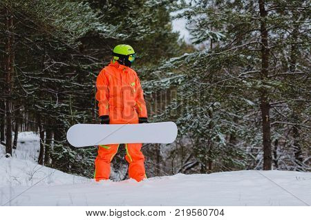 Snowboarder dressed in orange suit posing in winter forest