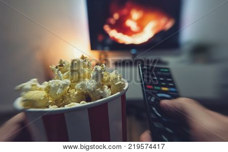 Pov shot from a hand holding a TV Remote control and Popcorn Box in his hand to watch a Movie at Home. ideal for websites and magazines layouts
