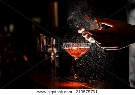 Bartender in black apron and blue shirt splitting pieces of ice by little piolet at a bar counter