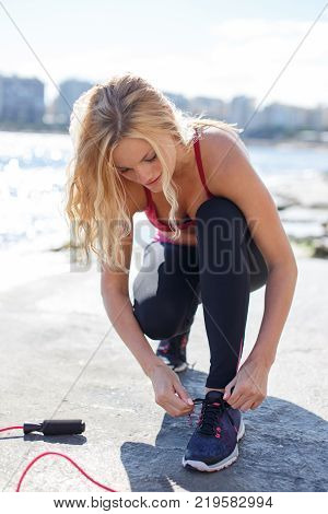 Young fit blonde woman tie shoelace before outdoor workout