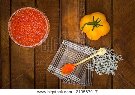 Red caviar in glass jar with gold spoon close up. Sea food. Healthy eating. Diet. Wooden rustic background. Top view. Selective focus
