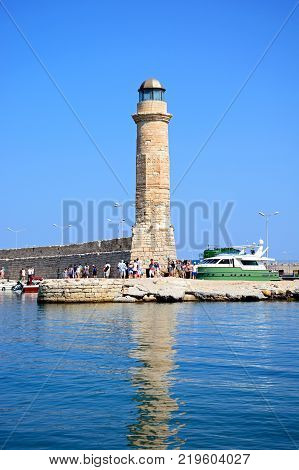 RETHYMNO, CRETE - SEPTEMBER 15, 2016 - View of the lighthouse with tourists walking along the harbour wall Rethymno Crete Greece Europe, September 15, 2016.