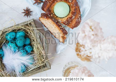 Traditional Greek Easter bread - tsoureki sliced in Easter decorations with painted blue quail eggs in the nest and flowers. Easter Festival concept.
