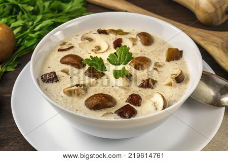 A closeup photo of a plate of a mushroom cream soup with champignons, cremini, fresh parsley, and pepper, on a dark rustic background