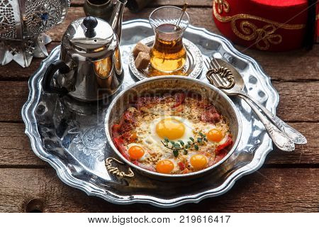 Fried egg with cured meat, traditional turkish breakfast, served in metal dishware, rustic.
