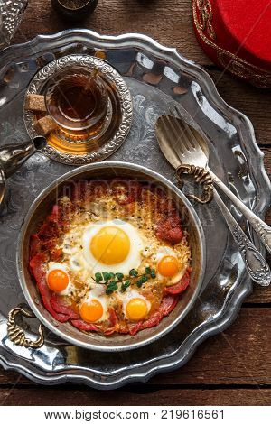 Turkish cured beef and fried eggs in copper pan, traditional breakfast, top view.