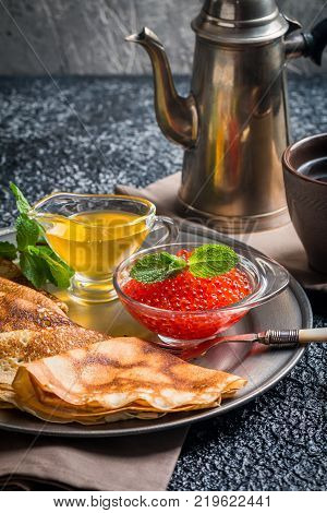 Yeast pancakes, traditional for Russian pancake week witn red cavier and honey on metal plate, black background
