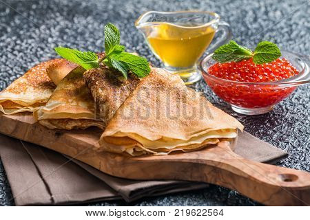 Yeast pancakes, traditional for Russian pancake week witn red cavier and honey on wooden cutting board, black background
