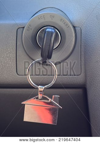 Car key in ignition. Start stop or accelerate engine. House shape keyfob on vehicle dashboard background. Real estate concept.