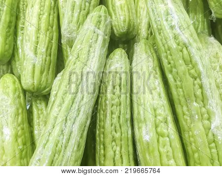 Closeup surface pile of fresh green bitter cucumber in plastic rap for sell textured background