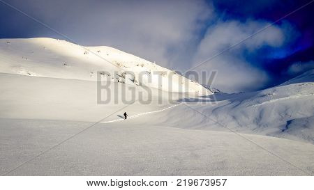 Early morning sun breaking through over a fantastic mountain landscape covered with a lot fresh snow. There is a snowshoe hiker following a new trail through this majestic landscape