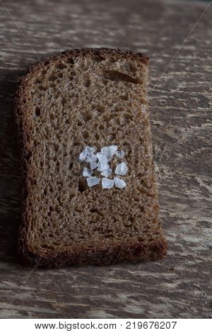 piece rough rye bread with coarse salt on a wooden background macro shot