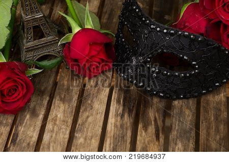red fresh roses with masque and eiffel tower on wooden table