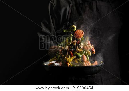 Chef cooking vegetables on a pan. Black background for copy text.