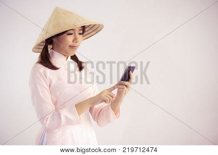 beautiful woman in pink dress and vietnam hat holding smartphone.