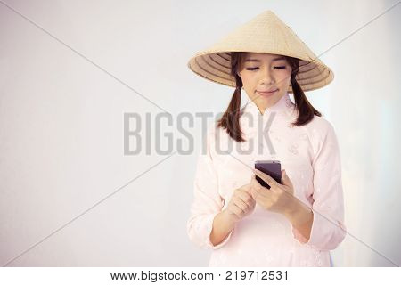 beautiful woman in pink dress and vietnam hat holding smartphone.