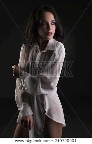 Beautiful brunette with long wavy hair wearing sexy shirt cropped portrait in dark room