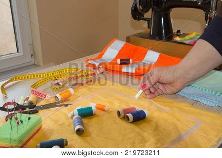 Close up of woman's hands drawing a pattern on yellow tissue. Measuring tape and sewing accessories. A tailor is laying out a dress. Sewing layout tailoring concept