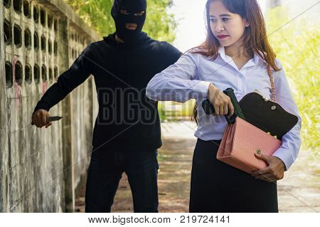 Beautiful young woman hiding gun safety self from robber thief mask danger with knife for stop gangster on street. Crime and robbery concept.