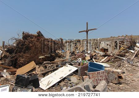 An unrecognizable pile of rubble and a makeshift cross tied with a ripped American flag lifted above the damage is all that is left after a home was ripped apart by an EF5 Tornado.