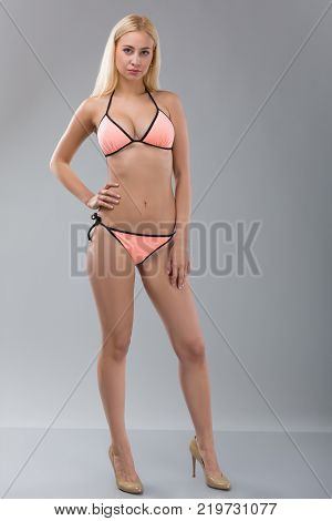Young sexy blonde woman in pink swimsuit over grey background. Model test