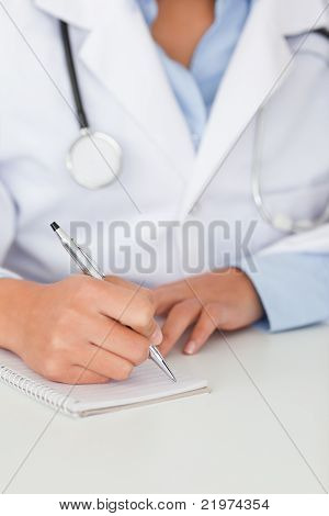 Ung kvinna läkare med ett stetoskop skriftligt på ett anteckningsblock