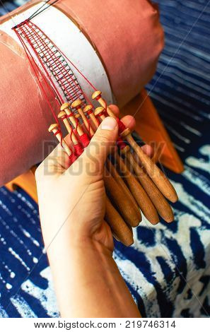 Making bobbin lace in traditional way. Detail on hands holding wooden bobbins with wound thread. Pillow lace.
