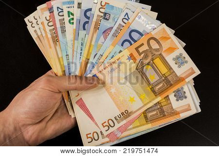 Human hand holding money - fifty-twenty-ten euro banknotes isolated on a dark gray background