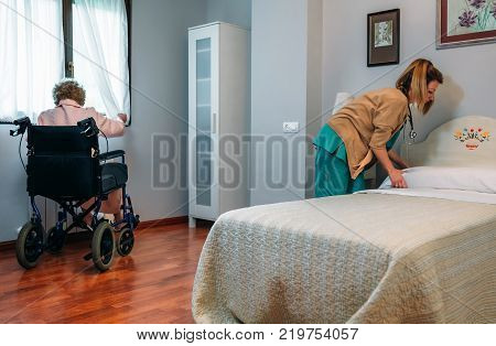 Caregiver making the bed of an elderly patient in a nursing home