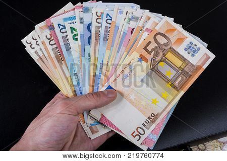 Human hand holding money - fifty-twenty-ten euro banknotes isolated on a dark gray background
