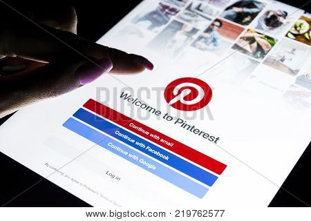 Sankt-Petersburg Russia December 21 2017: A woman's hand is touching screen on tablet iPad Pro at night with Internet service Pinterest on the screen. Pinterest application on tablet computer screen.