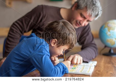 Young little shoolboy solving mathematics homework with father cooperation in family parenthood