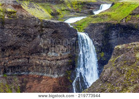 Gloomy foggy July day in Iceland. High waterfall Hayfoss in a picturesque and dangerous tundra canyon. The concept of extreme and phototourism