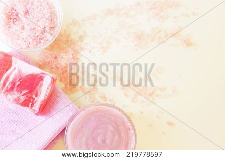 Luxirious spa facilities- glass clear bowls with bath salt and pink face or body cream, pink towel with a bar of soap, salt grains on the table, top view. Space for a text or product display.