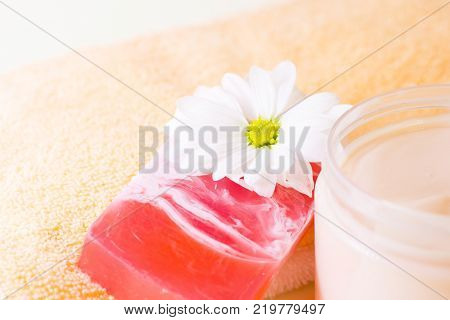 Facecare and bodycare concept. A bar of fruit soap, a fresh cut camomile flower, a container with smooth cream and clean towels, close up. Space for a text or product display.