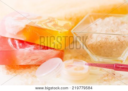 Facecare and bodycare concept. A close up of a bowl of fragrant bath salt and bars of fruit soap, a small container with body or face cream and a dropper. Space for a text or product display.