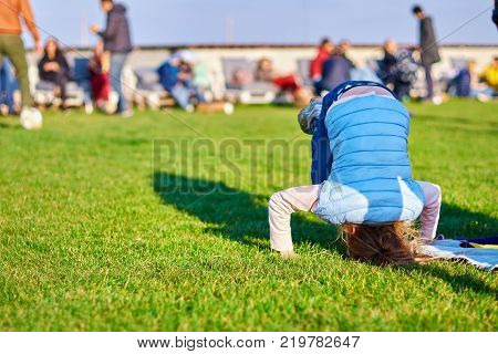 little girl standing on her head on the grass in the park. Childhood concept ready for your text logo or symbols.