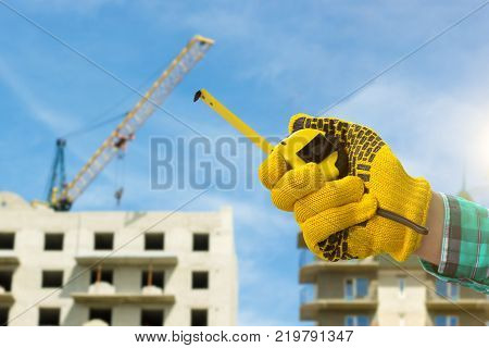 Roulette in the hand with a protective glove against the background of a house under construction.