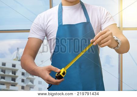 Master hand holds the tape measure in the background of a house under construction outside the window.