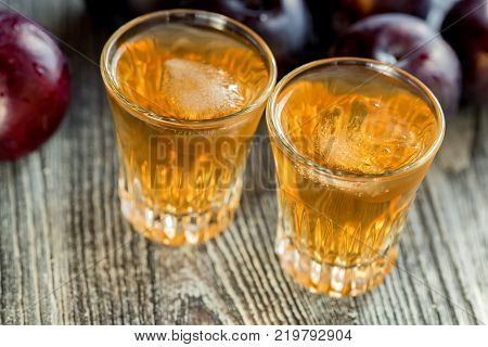 Plum liqueur or slivovitz, plum rakia with fresh and tasty plum on rustic wooden background