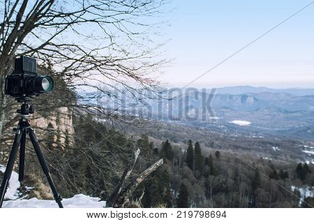 Retro professional camera on a tripod, outdoor wildlife photography. Mountains, forest background.