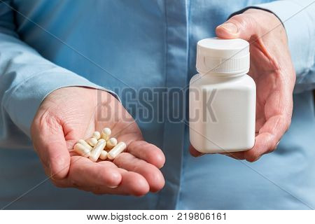 White medication capsules of glucosamine healthy supplement pills in woman palm hand demonstrate one pill.